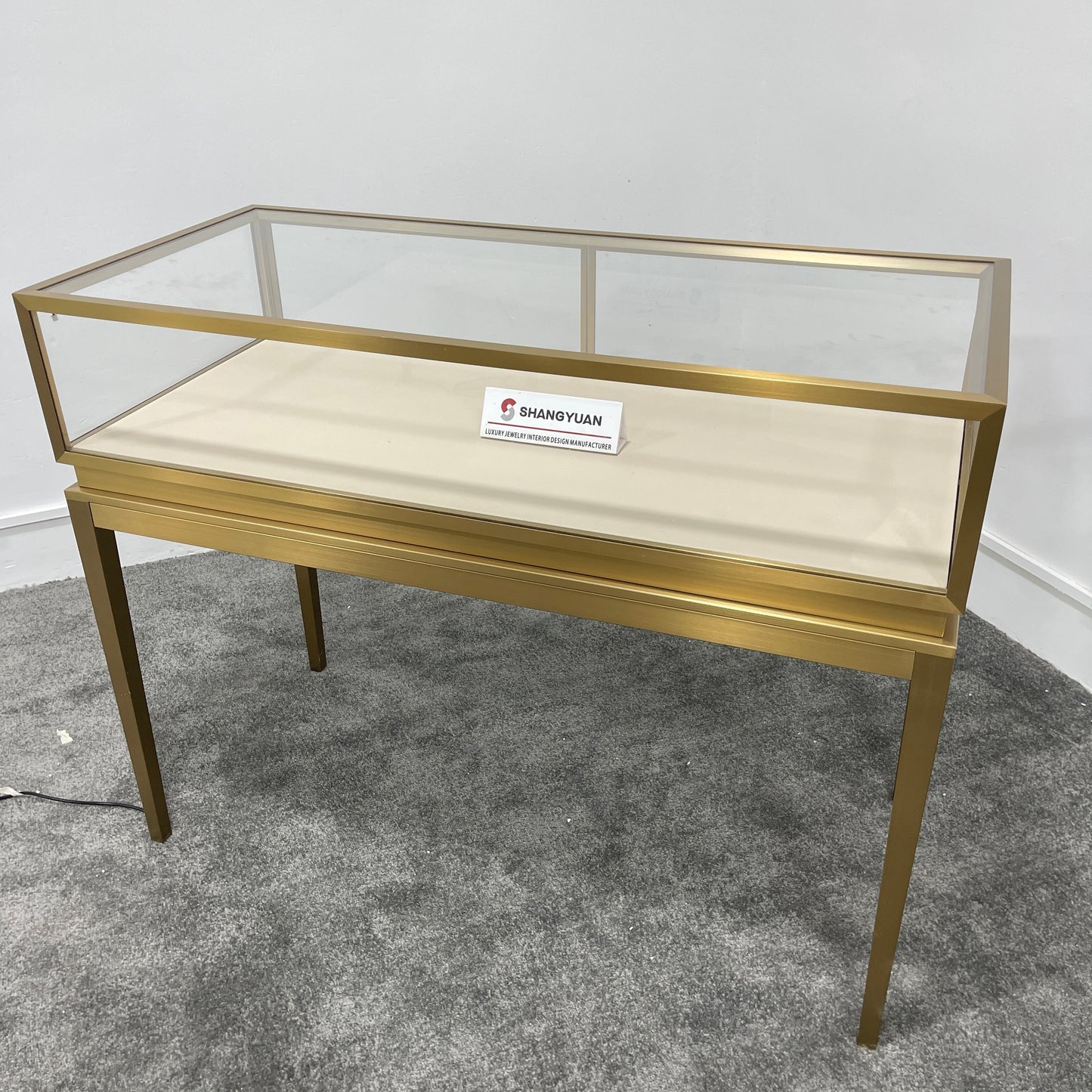 Full side view of freestanding gold stainless steel jewelry display case with glass top and slim tapered legs