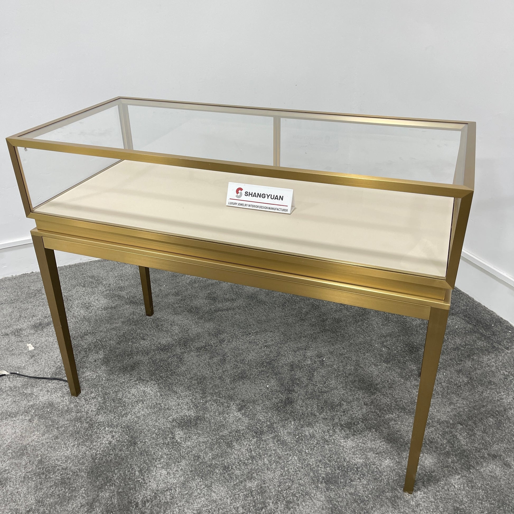 Full side view of freestanding gold stainless steel jewelry display case with glass top and slim tapered legs