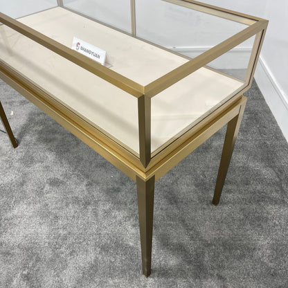 Close-up corner detail of gold brushed stainless steel jewelry display case with tempered glass top and cream velvet interior