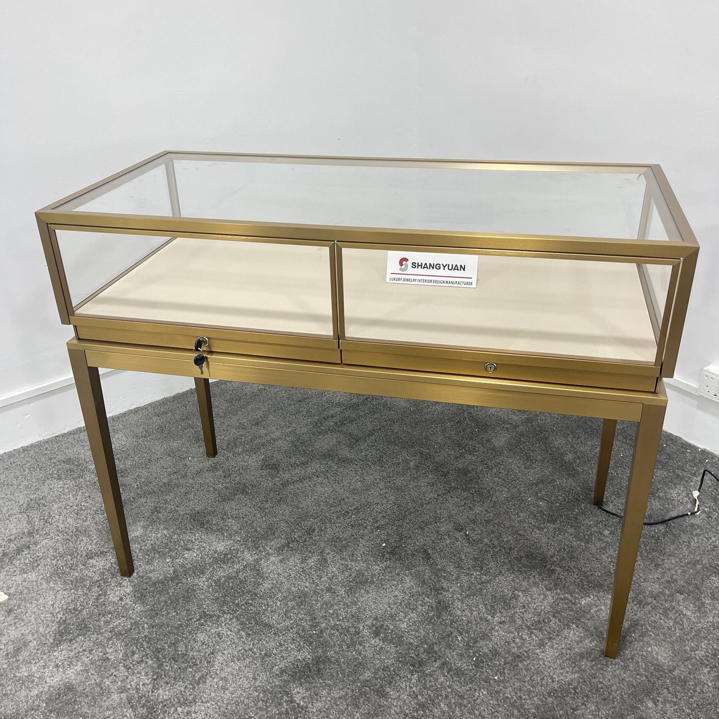 Side angle view of gold stainless steel jewelry showcase with clear glass panels and cream velvet display surface