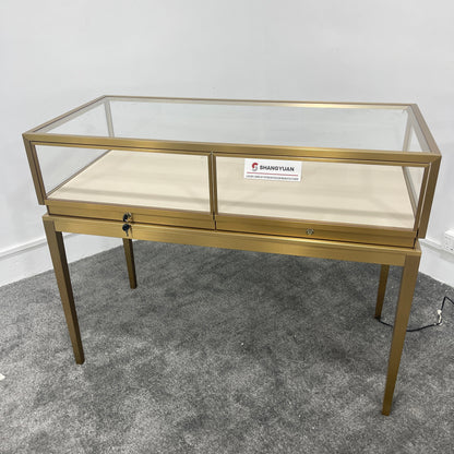 Side angle view of gold stainless steel jewelry showcase with clear glass panels and cream velvet display surface