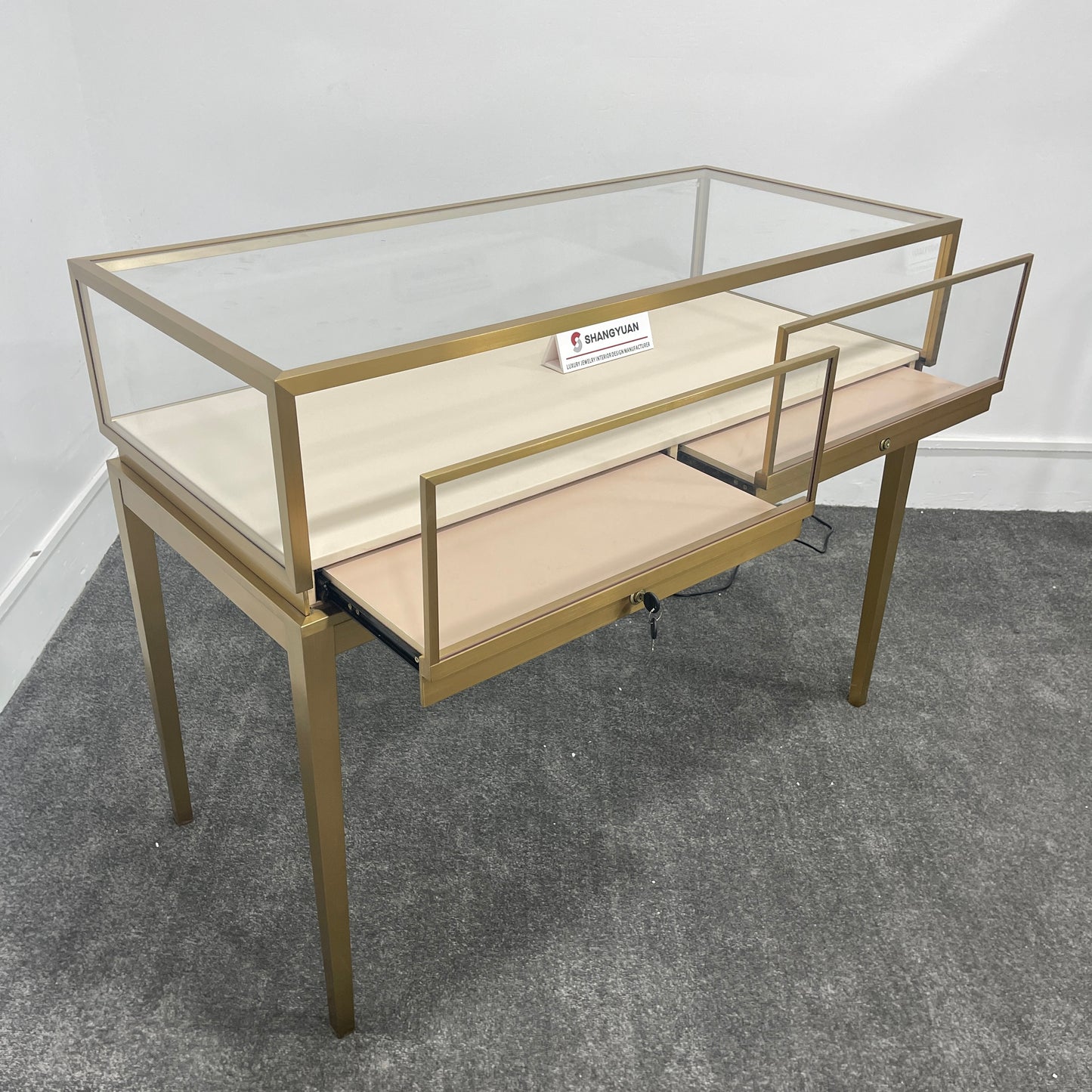 Gold jewelry display case with sliding glass door open showing lockable drawer and storage shelf underneath